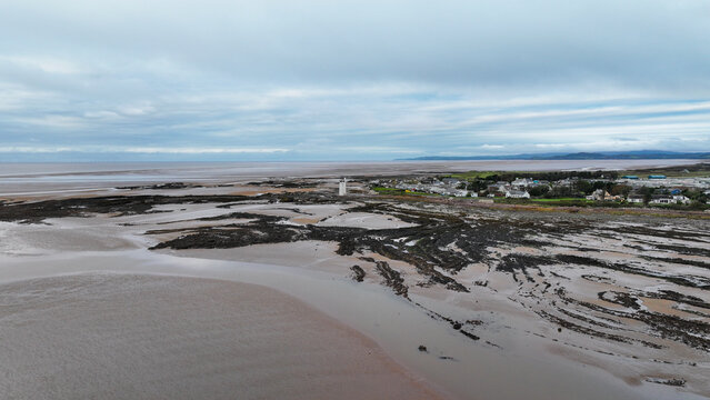 Aerial view of Southerness Lighthouse on the rocky coast with the village and Solway Firth in the background under a cloudy sky, Southerness, Scotland, United Kingdom.
