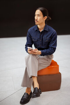 Man Sitting on a Stool While Using a Smartphone Indoors