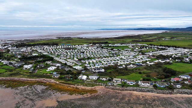 Aerial view of Southerness holiday park with rows of white caravans along the coastline, green fields, and sandy beach in Southerness, Scotland, United Kingdom.