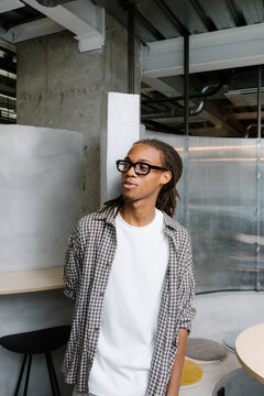 Smiling Black freelancer with dreadlocks leaning against a wall.