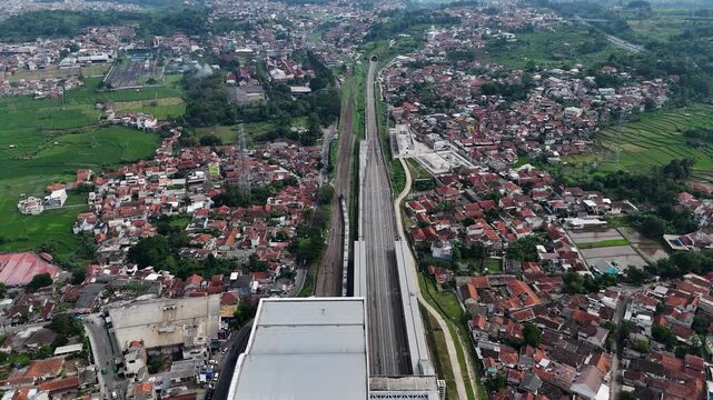 Aerial view of Stasiun Kereta Cepat Padalarang with high-speed rail tracks, surrounding residential neighborhoods, and green fields in Padalarang, West Java, Indonesia.