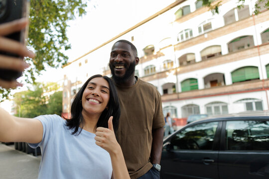 Diverse couple taking selfie gesturing thumbs up