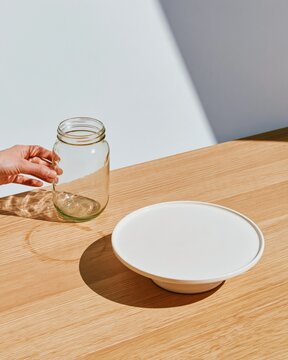 Glass jar and white cake stand on a light wooden table in soft daylight, clean tabletop mockup with copy space for branding