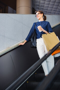 Woman Going Down Escalator With Shopping Bags and Coffee