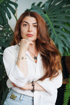Woman in White Shirt with Hand on Chin by a Monstera Plant