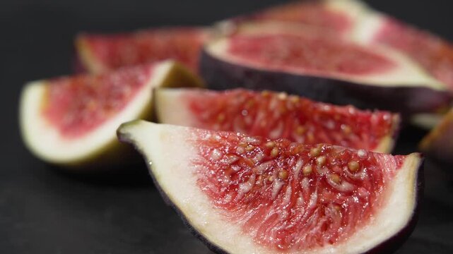 Low angle close-up of fresh fig wedges slowly rotating on a dark surface with shallow depth of field, showing seeds and pulp.