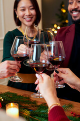 Fototapeta premium Vertical shot of diverse young adult friends toasting with red wine glasses during holiday celebration, useful for hospitality marketing and seasonal advertising campaigns