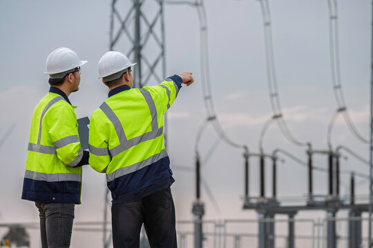 Electrical engineering team reviews high voltage substation infrastructure during routine inspection, representing power transmission, grid reliability, maintenance, and utility safety.