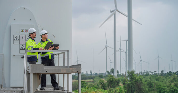 Renewable energy engineering team performs a wind turbine inspection with digital devices, supporting maintenance planning, industrial safety, and sustainable electricity generation.
