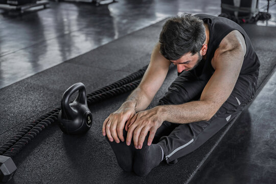 Fitness man performs a seated hamstring stretch on an exercise mat after training, supporting flexibility, muscle recovery, mobility, and post workout cooldown.