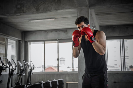 Fit athletic young man throwing a punch wearing red boxing gloves during an intense training session inside a modern gym showcasing dedication to physical fitness and healthy lifestyle.