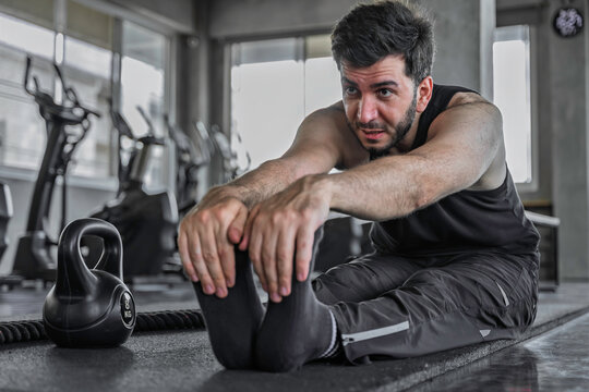 Fitness man performs a seated hamstring stretch on an exercise mat after training, supporting flexibility, muscle recovery, mobility, and post workout cooldown.