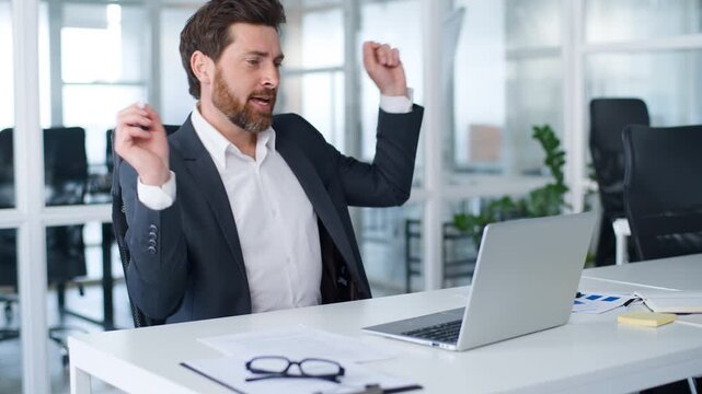 Positive Caucasian mature business man writing notes in document dancing using laptop technology listening music during work process businessman write typing computer enjoy song audio male in office