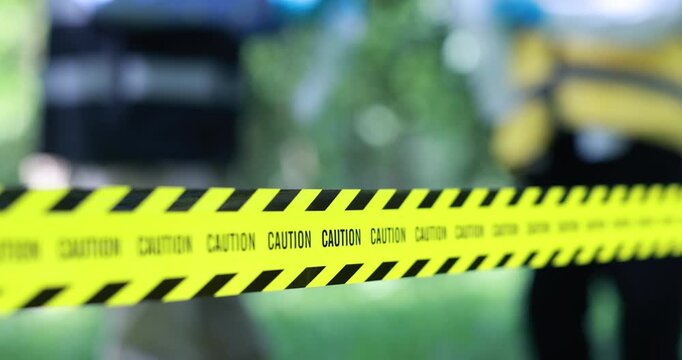 Yellow caution tape blocks access to a blurred outdoor work area with a construction vehicle in the background.
