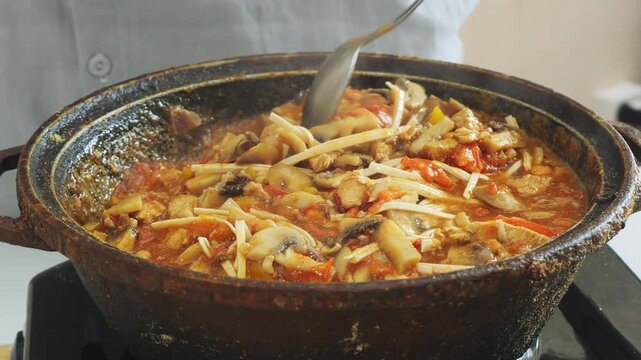 Vegetables simmer in a deep cast-iron skillet with chicken and udon, stirring