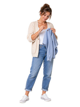Woman mending a blue shirt by hand, wearing glasses, a beige cardigan, and cuffed jeans while standing, isolated on transparent background