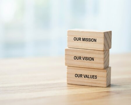 Three stacked wooden blocks on a light wooden surface, each engraved with the words our mission, our vision, and our values in black lettering