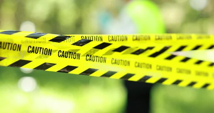 Yellow caution tape stretches across a sunny outdoor area, creating a clear safety barrier against a soft green blurred background.