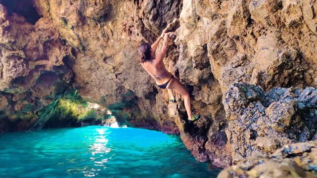 Woman Deep Water Soloing Climbing on Sea Cave Cliff with Turquoise Water