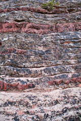 Vertical close-up of layered stone with red, gray and dark mineral bands creating a striking natural geological texture and abstract background. © MariaHemi