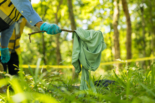 Volunteer wearing protective gloves removes discarded fabric from grassy woodland using a branch, highlighting outdoor cleanup, environmental care, and litter prevention.