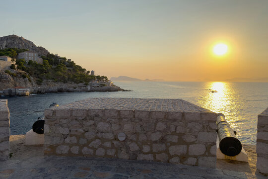 Iron cannons on weathered stone bastion above rocky coast at sunset in Hydra, Greece