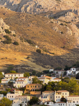 Whitewashed houses with terracotta roofs below rugged mountainside in Hydra, Greece, at sunset