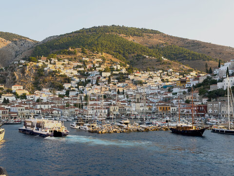 Ferries, yachts and sailboats fill Hydra harbor below hillside homes on summer evening, Greece