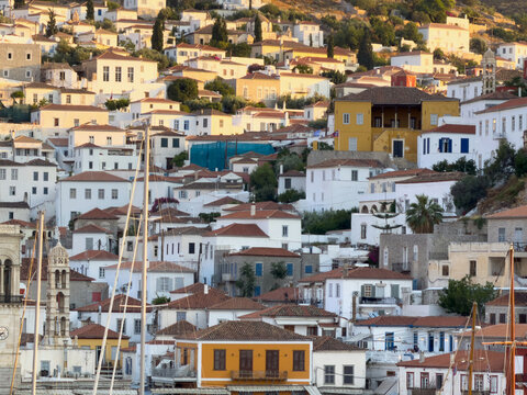 Whitewashed hillside houses and sailboat masts at Hydra harbor, Greece, in evening light
