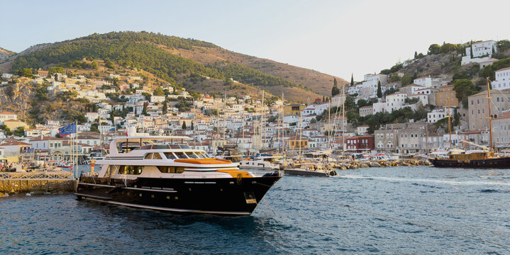 Luxury motor yacht moored at Hydra waterfront below whitewashed hillside buildings in Greece