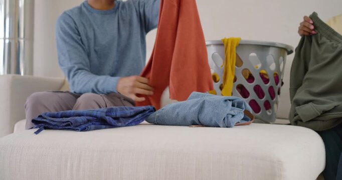 African American couple starting with laundry basket, folding clothes and sorting stacks on couch
