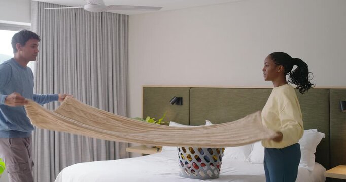 African American couple grabbing corners folding beige throw on bed placing folds into laundry bin