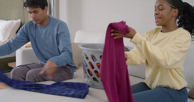 Full laundry basket urging African American couple taking clothes, folding into stacks on ottoman
