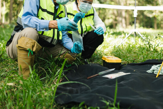 Environmental workers in protective clothing collect a field sample from grass beside a black tarp and testing tools outdoors