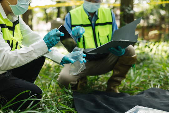 Environmental workers in protective clothing collect and analyze water samples outdoors in a forest, using safety equipment, containers, and a laptop for field research.