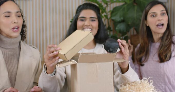 Diverse women unboxing delivered parcel in lounge, pulling inner box and black zip case, examining