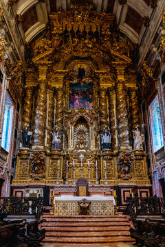 View inside Porto Cathedral showing central nave with stone arches wooden benches and ornate golden altar. Historic religious architecture with visitors sitting in quiet atmosphere.