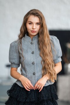 Elegant woman model posed indoors in bright neutral studio, wearing gray buttoned jacket with decorative buttons and long wavy light brown hair(1)4/7/2026 6:10 PM