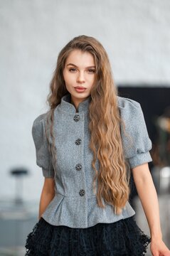 Confident close up portrait of woman in gray buttoned wool coat with long wavy hair indoors under soft natural light, subtle makeup, neutral background fashion editorial