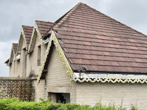 old abandoned brick house with brown tiled roof, weathered decorative white wooden fascia boards, exterior architectural view, vintage real estate concept with copy space