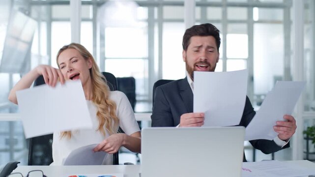 Two happy active business colleagues throwing papers singing dancing celebrating complete paperwork feeling free at office table Caucasian businessman with businesswoman throw documents sing dance