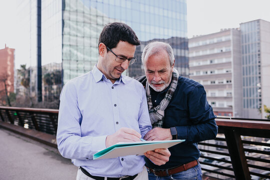two Adult Hispanic Business men Reviewing Documents together Outdoors in winter morning in city, Latin manager and employee 