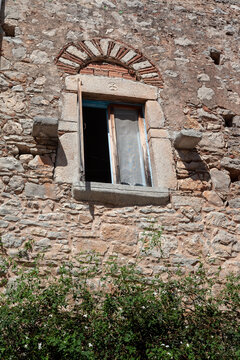 Traditional stone building with a wooden casement window, stone surrounds (jambs and sill), and an arched lintel featuring alternating stone and brickwork in Chios island, Greece
