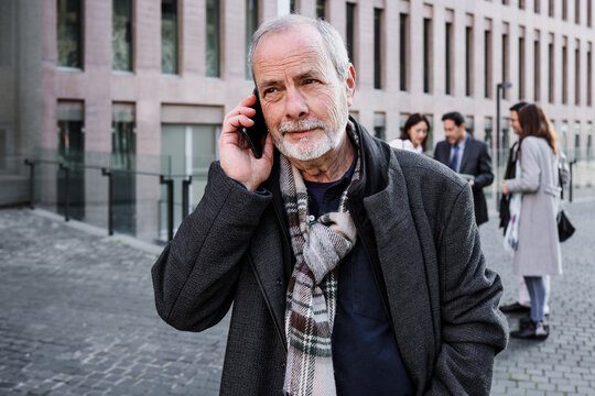 hispanic senior businessman talking on phone in a call outdoors in city, mature or elderly man using cellphone in cityscape 
