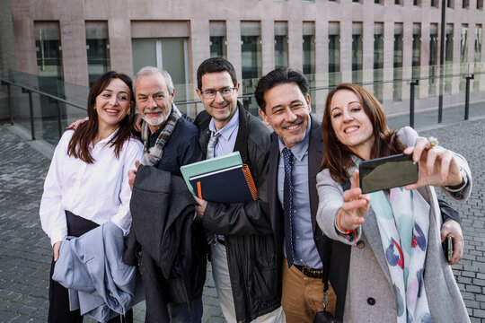 group of hispanic business people taking a selfie together outside office building and looking at the camera smiling.