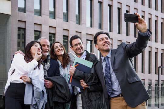group of hispanic business people taking a selfie together outside office building and looking at the camera smiling.