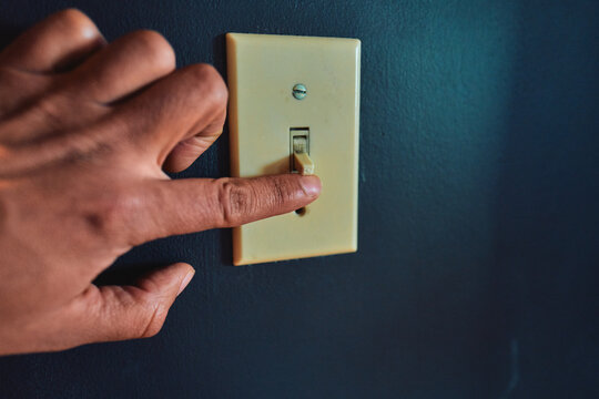 Hand Flipping a Toggle Light Switch on a Dark Blue Wall
