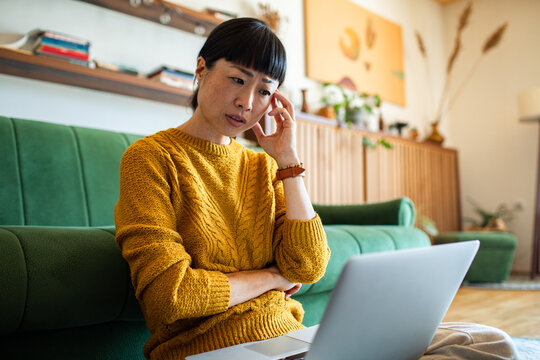 Concerned woman looking at laptop on living room sofa