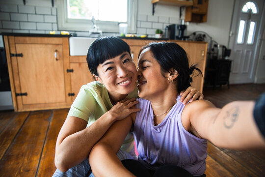 Woman kissing partner's cheek during kitchen selfie