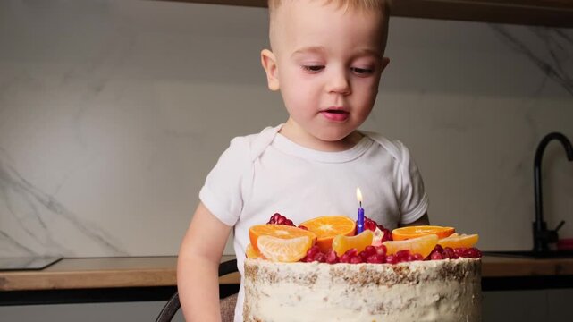 Little boy celebrating his birthday with fruit cake and single candle in kitchen indoor space